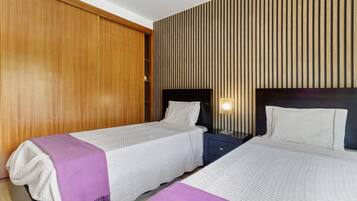 Habitación de hotel con dos camas, paneles de madera en las paredes, una mesita de noche con lámpara y un armario.