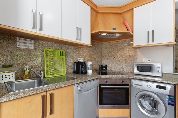 A compact kitchen with a dishwasher, microwave, oven, and a green cutting board on the countertop.