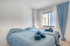 A hotel room with two beds, a window with curtains, and a lamp on the nightstand.