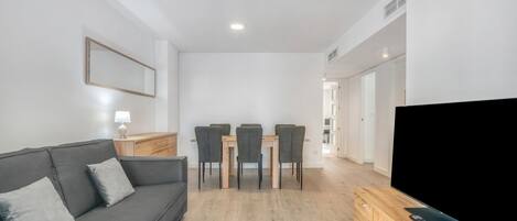 A modern living room with a sofa, dining table, chairs, and a flat-screen TV.