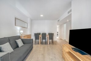 A modern living room with a sofa, dining table, chairs, and a flat-screen TV.
