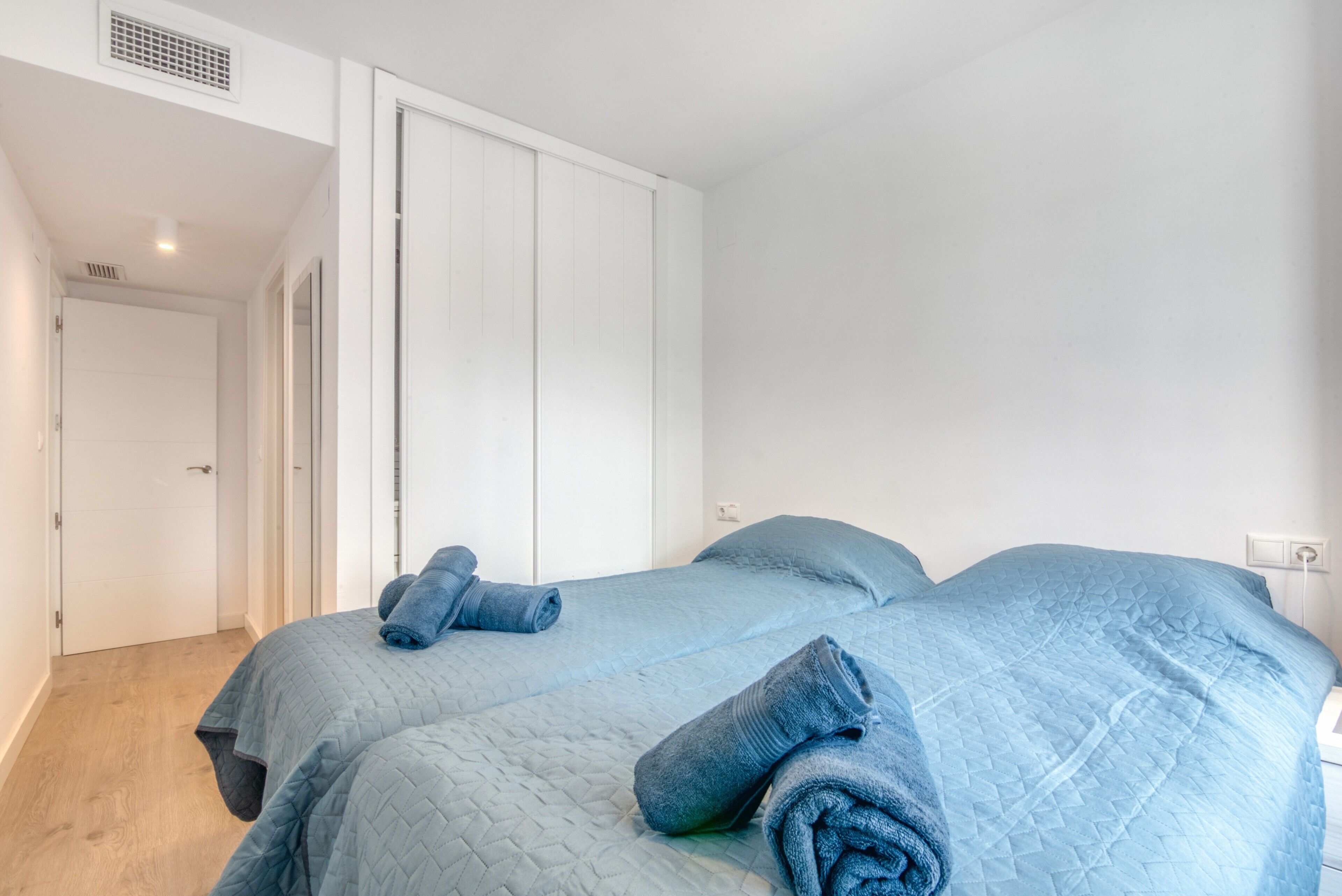 A bedroom with two beds, a white wardrobe, and a door leading to another room.