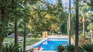 A swimming pool surrounded by palm trees and lounge chairs, with a stone wall and a sign indicating pool depth. - Apartment 'La Quinta Golf' with Sea View, Wi-Fi and Air Conditioning (Unknown)