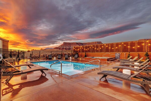 A rooftop pool with lounge chairs, a pool ladder, and a view of mountains.