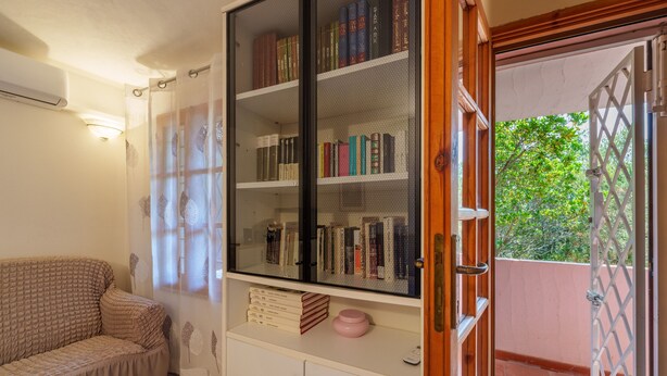 Ein Zimmer mit einer Couch, einem Bücherregal, einem Schrank und einer Tür, die nach draußen führt.