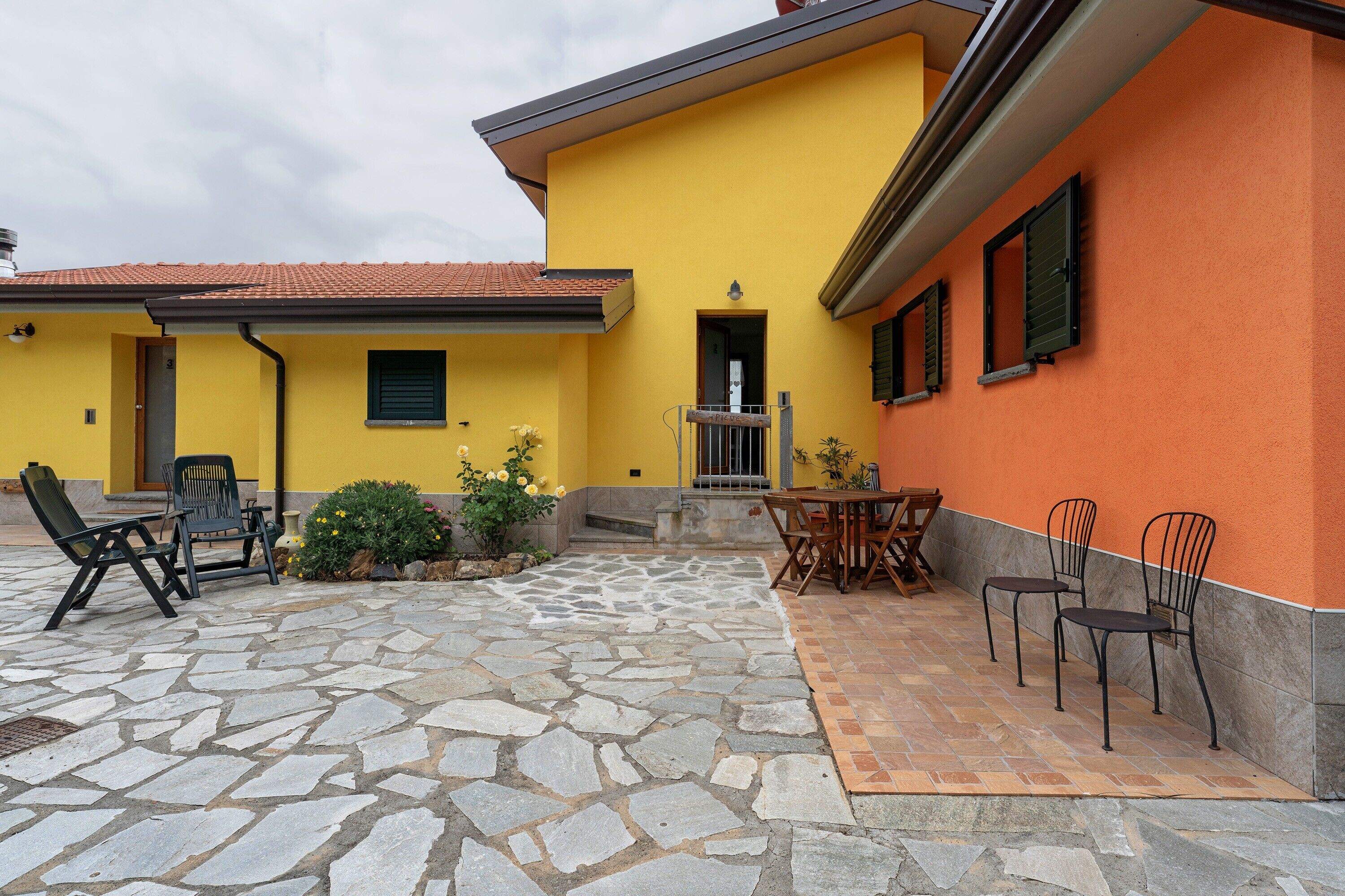 Ein Innenhof mit Steinpflaster, Sitzmöglichkeiten im Freien und einem gelben Gebäude mit orangenen Wänden.