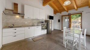 Una cocina moderna con armarios blancos, un refrigerador de acero inoxidable y un comedor con mesa de vidrio y sillas blancas.