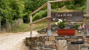 Ein Holzschild mit der Aufschrift 'PARKING' und einem nach links zeigenden Pfeil, eine Steinmauer und ein Blumentopf mit Blumen.