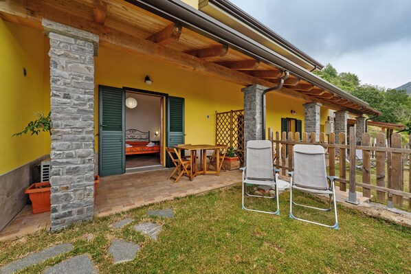 Eine überdachte Terrasse mit Steinpfeilern, einem Holztisch und zwei Stühlen.
