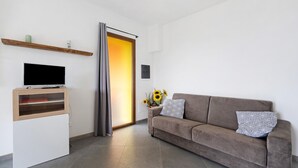 Ein modernes Wohnzimmer mit einem Flachbildfernseher, einer Holzregal, einem Sofa mit gemusterten Kissen und einer Tür zu einem hellen Raum.