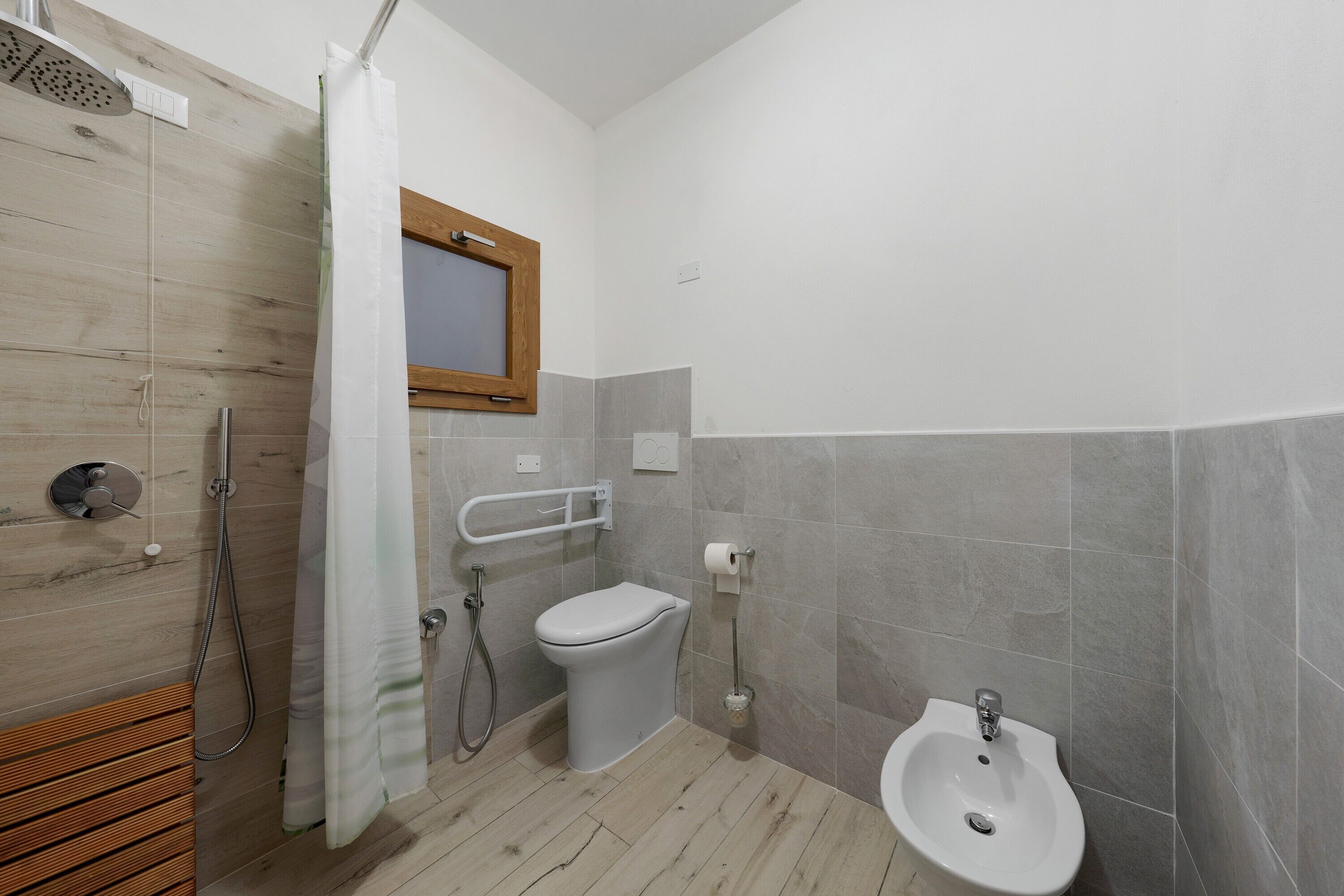 A bathroom with a shower, toilet, bidet, and wooden paneling.