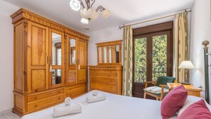 A hotel room with a large bed, wooden wardrobe, and a balcony with a view of trees.