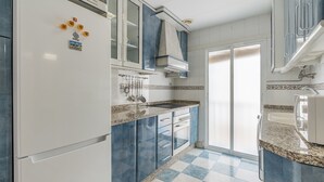 A kitchen with a white refrigerator, blue cabinets, a double sink, and a patterned floor.