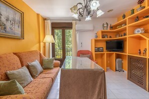 Una sala de estar con un sofá, una mesa de centro de vidrio, un televisor y una estantería.