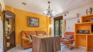 A living room with a sofa, a table, a chair, a chandelier, and a shelf with decorative items.