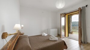 Un dormitorio con cama, mesita de noche, lámpara, radiador y vistas al exterior.