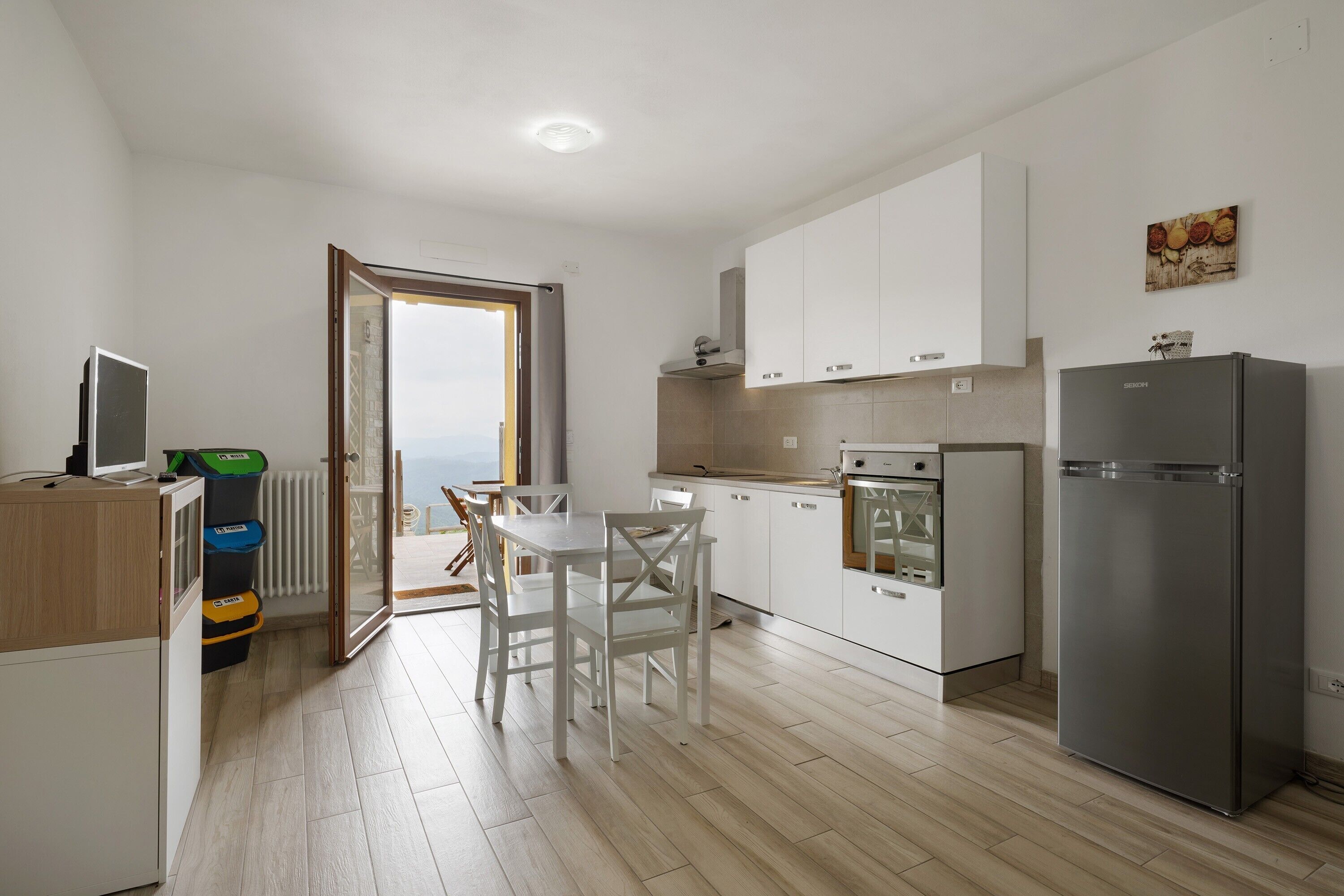 Una cocina moderna con armarios blancos, un refrigerador de acero inoxidable y una zona de comedor con sillas blancas.