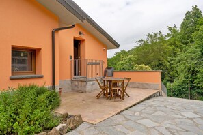 Et hus med orange facade, en terrasse med bord og stole, og en lille balkon.