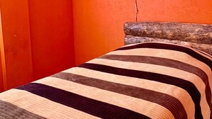 Une chambre aux murs orange, avec une tête de lit en bois et une couvre-lit à rayures.
