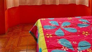 Une pièce avec un lit, une fenêtre ornée de rideaux légers et un mur rouge.