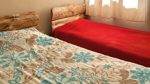 Une chambre avec deux lits, l’un recouvert d’une couvre-lit à motifs floraux et l’autre d’une couverture rouge.