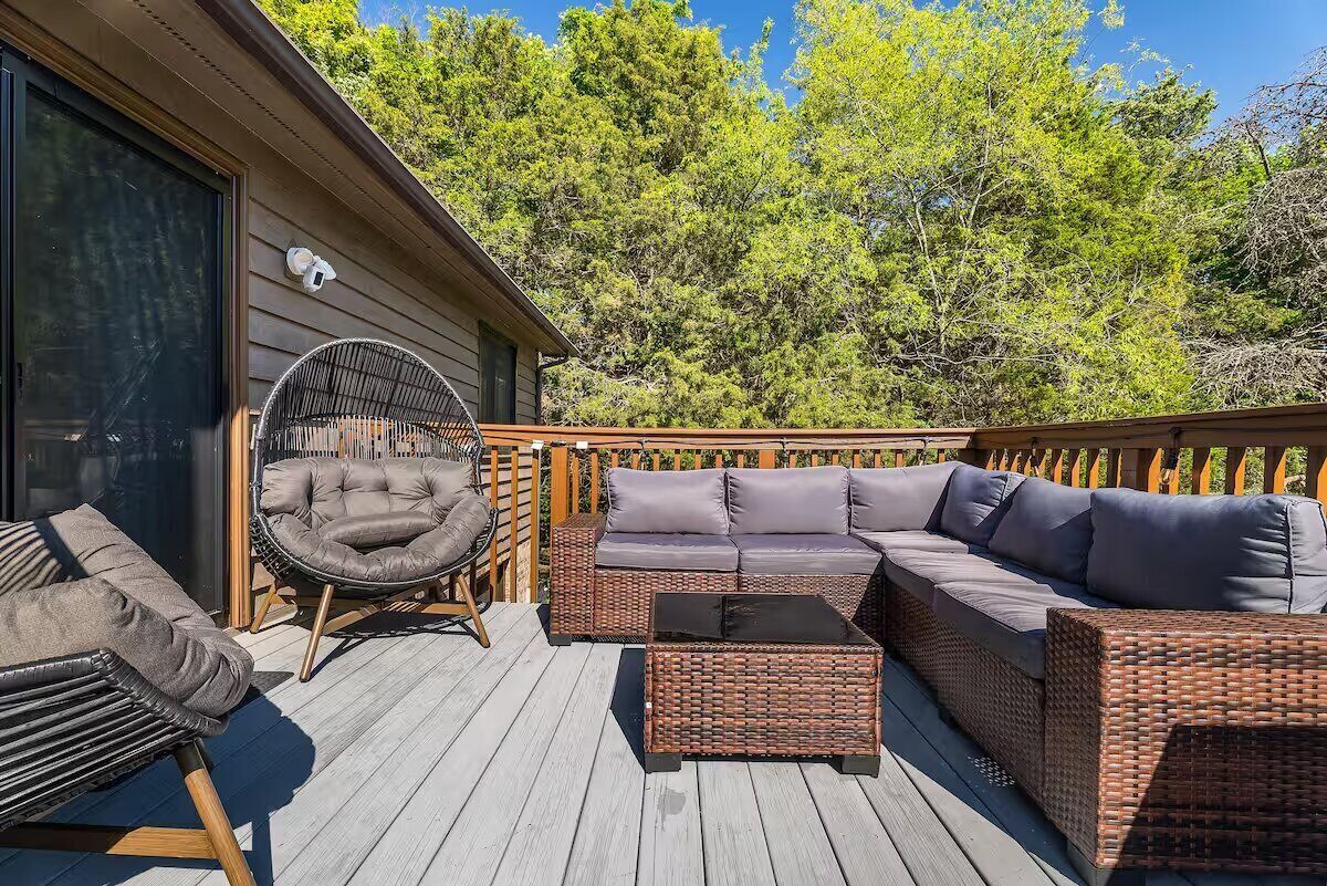 A deck with wicker furniture, including a sofa and chairs, and a glass coffee table.