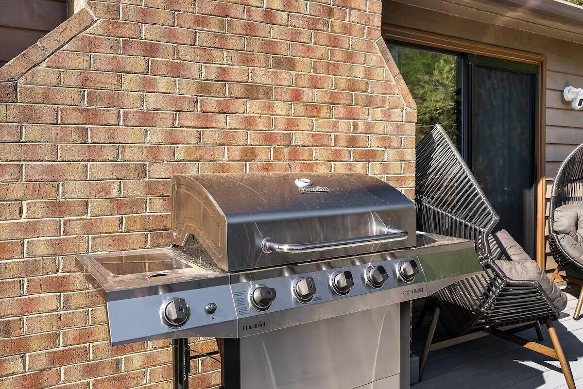 A Char-Broil gas grill with four burners, a glass lid, and a chimney, installed against a brick wall.