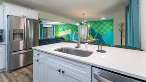 A modern kitchen with white cabinetry, a stainless steel refrigerator, and a colorful geometric wall mural. - Neon Dream Lodge! Pickleball, Hot Tub, Theater (McGaheysville)