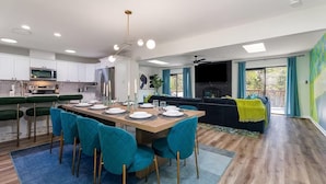 A modern kitchen with white cabinets, a dining area with teal chairs, and a living room with a black sofa and a green blanket. - Neon Dream Lodge! Pickleball, Hot Tub, Theater (McGaheysville)