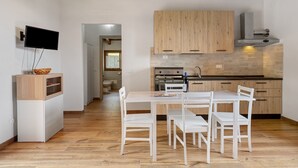 A modern kitchen with wooden cabinets, a built-in oven, and a dining area with white chairs. - Apartment 'Camera 1' with Mountain View, Private Terrace and Wi-Fi (Sasseta)