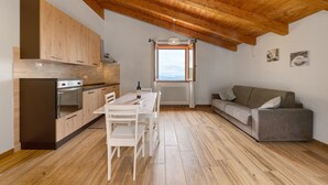 A modern kitchen with wooden cabinets, a dining table, and a sofa in a loft-style room with a wooden ceiling. - Apartment 'Camera 1' with Mountain View, Private Terrace and Wi-Fi (Sasseta)