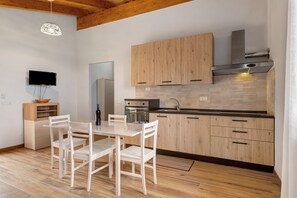 Uma cozinha moderna com armários de madeira, bancada preta e área de refeições com cadeiras brancas.