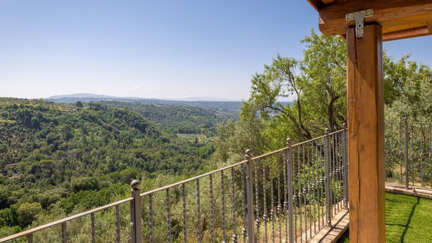 Un balcon en bois, doté d’une rambarde en métal, surplombe une vallée boisée.