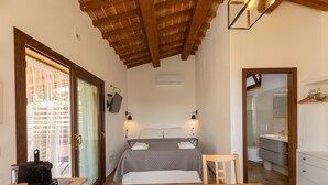 Une chambre à coucher avec un lit, des tables de chevet, un plafond en bois et une salle de bain visible à travers une porte ouverte.