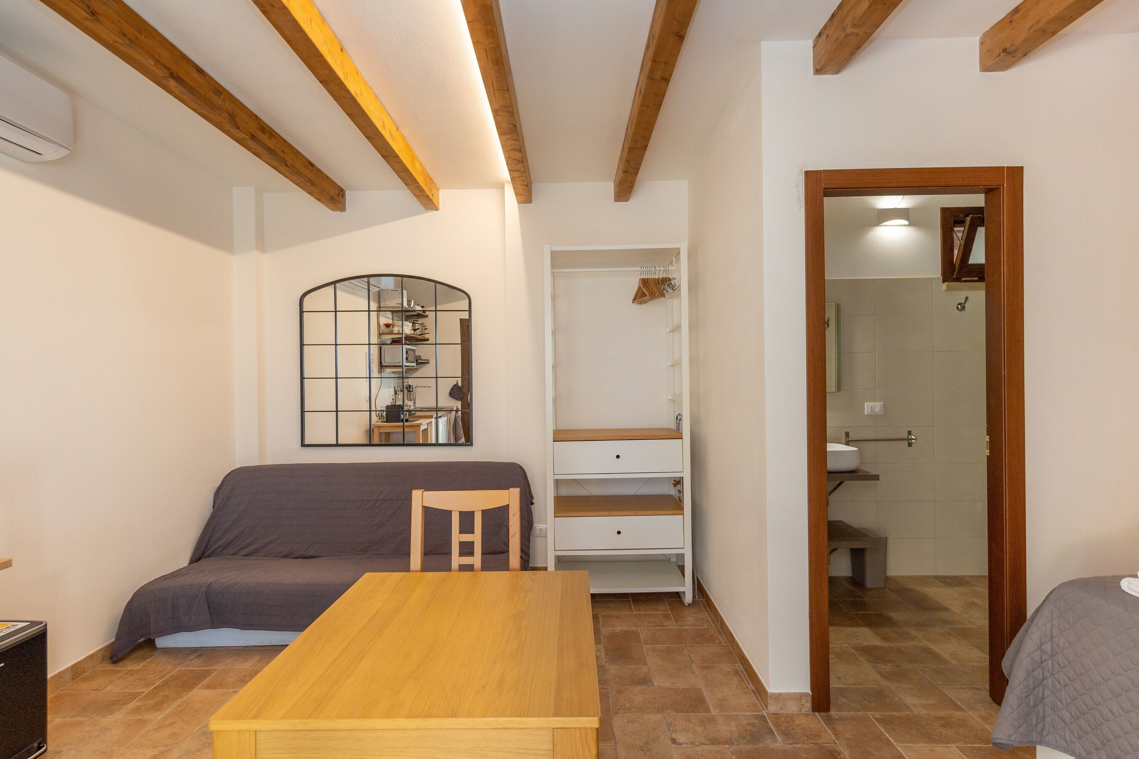 Une chambre à coucher avec un lit, une table en bois, une chaise, une armoire et une salle de bain visible à travers une porte ouverte.
