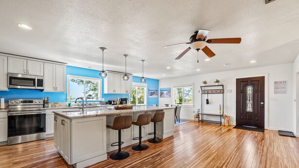 A modern kitchen with a large island, bar stools, stainless steel appliances, and a ceiling fan.