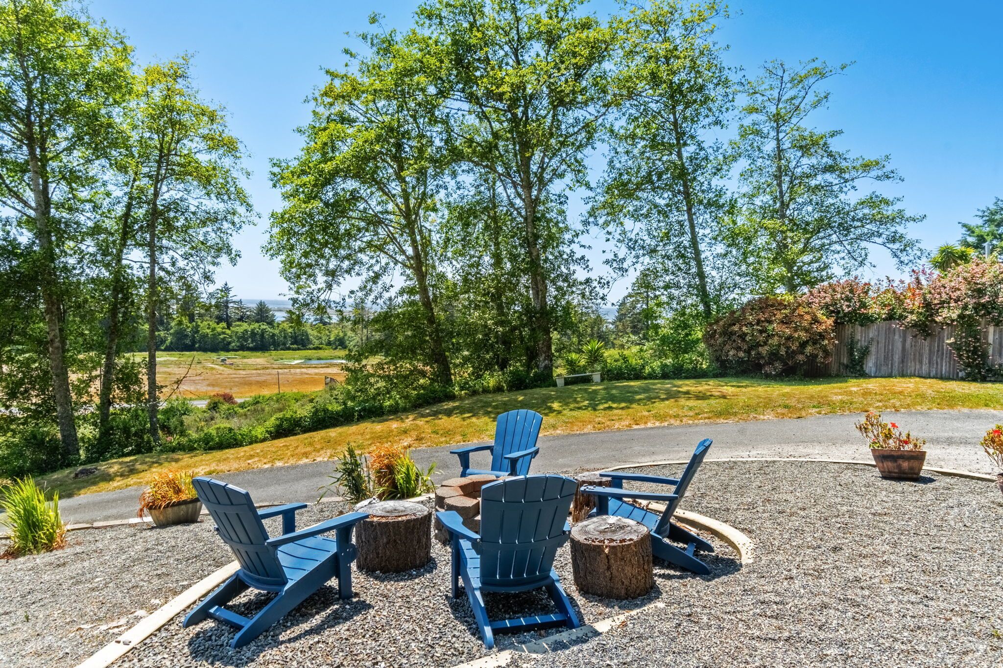 Un espace extérieur aménagé avec des chaises Adirondack et un foyer, entouré d’arbres et offrant une vue sur un paysage rural.
