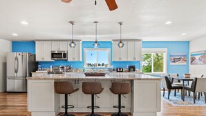 A modern kitchen with white cabinets, a large island with bar stools, and pendant lighting.