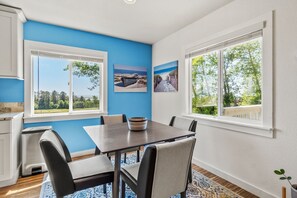 Un comedor con mesa y sillas, ventanas amplias y obras de arte en las paredes.