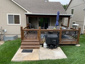 A covered patio with a grill, outdoor furniture, and a wooden deck. - 1 night or more. A Charming 3-bedroom-Spacious, Quiet, Comfortable Home (Lawrence)