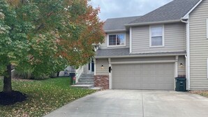 A two-story house with a garage, a front yard with a tree, and a driveway. - 1 night or more. A Charming 3-bedroom-Spacious, Quiet, Comfortable Home (Lawrence)