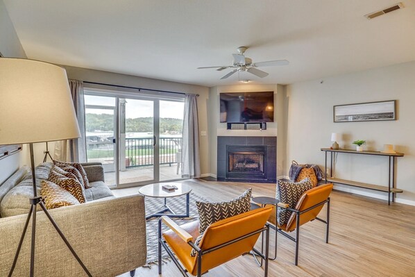 A living room with a fireplace, a ceiling fan, and a view of a lake through large sliding doors.