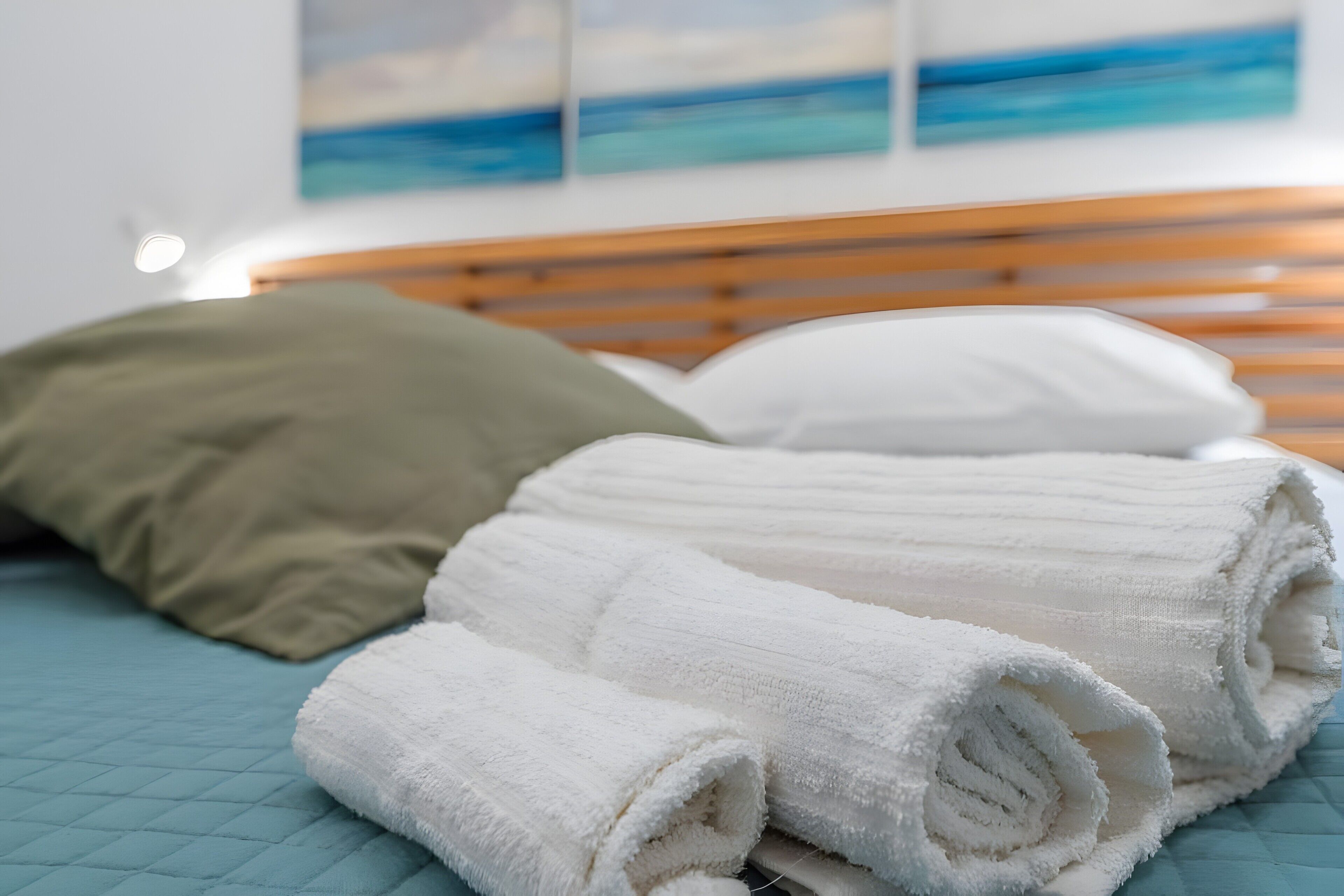 Una cama con un colchón azul acolchado, cabecera de madera y toallas blancas enrolladas.