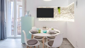 Un comedor con una mesa dispuesta para cuatro, un televisor montado en una pared texturizada y vistas a un balcón a través de una puerta corredera.