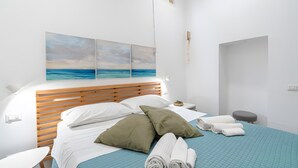 Una cama bien hecha con almohadas, un edredón azul y vista al mar a través de una ventana.