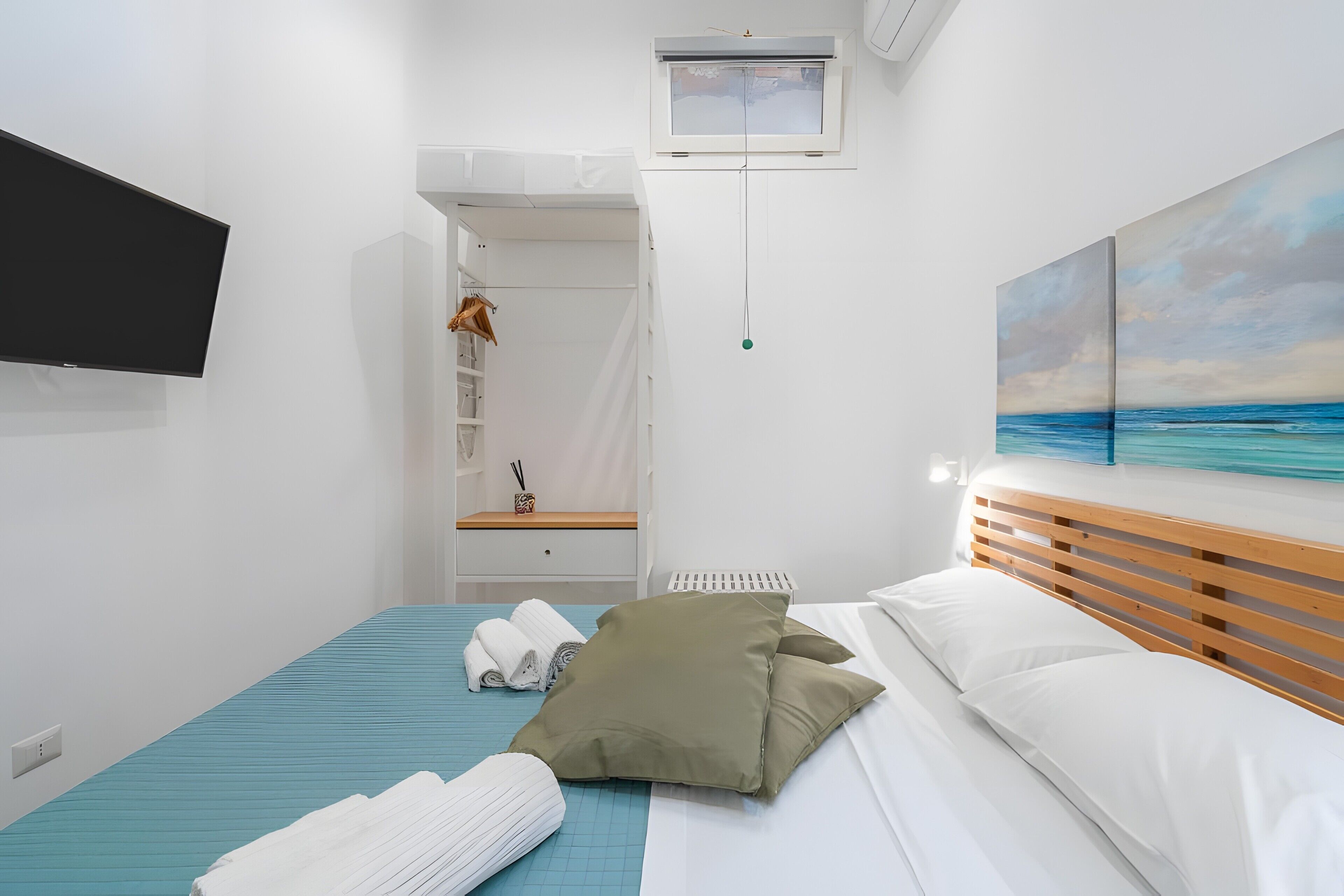 A hotel room with a bed, a TV, a painting, and a window.