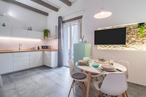 A modern kitchen with white cabinets, a wooden countertop, and a dining area with white chairs and a table set for two.