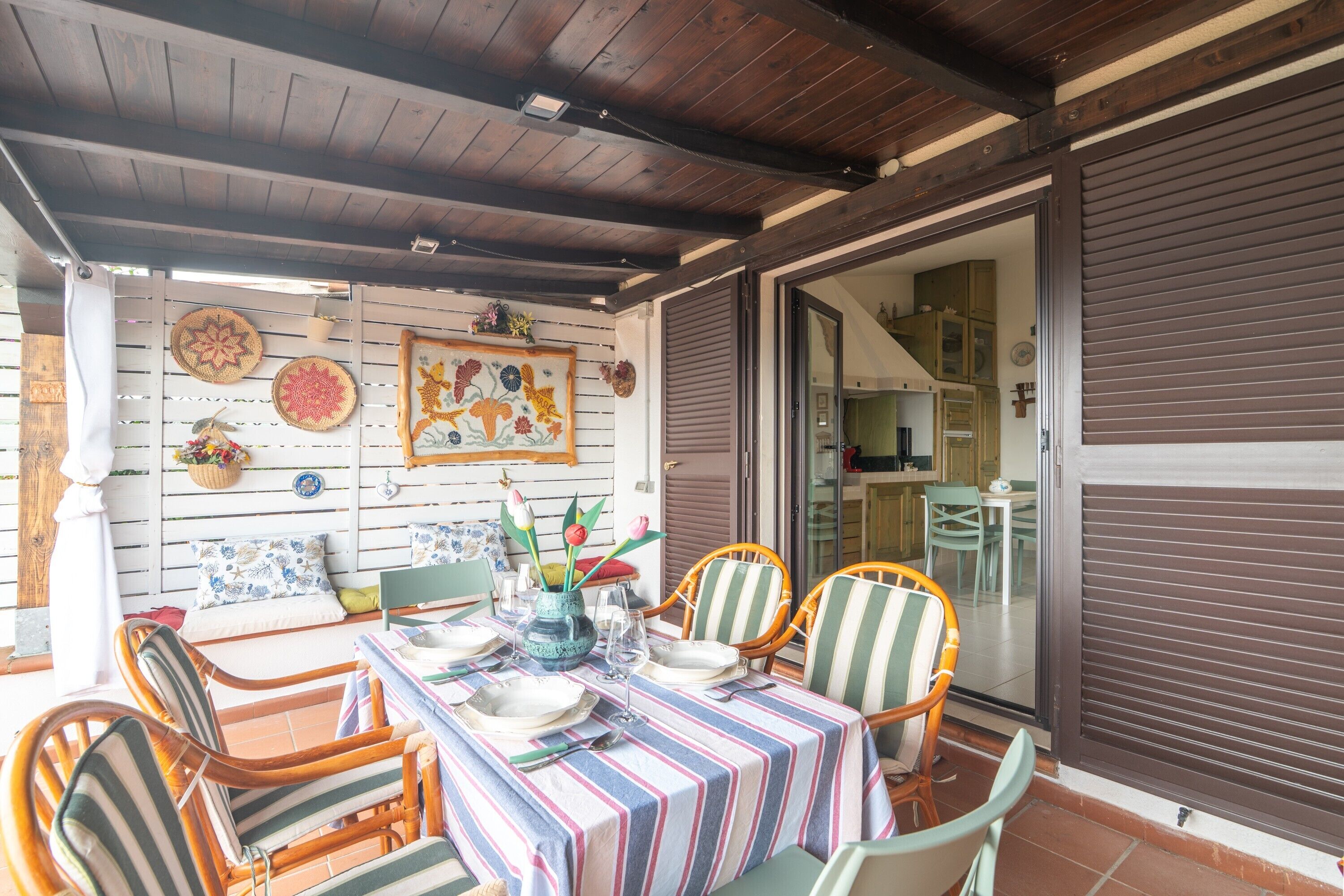 Une terrasse couverte avec une table dressée pour les repas, des chaises en osier et un mur décoratif agrémenté de divers objets.