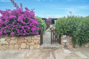 A stone wall with a gate, a stone pathway, and a building in the background. - Holiday Home 'Rosemary House' with Air Conditioning (Olbia)