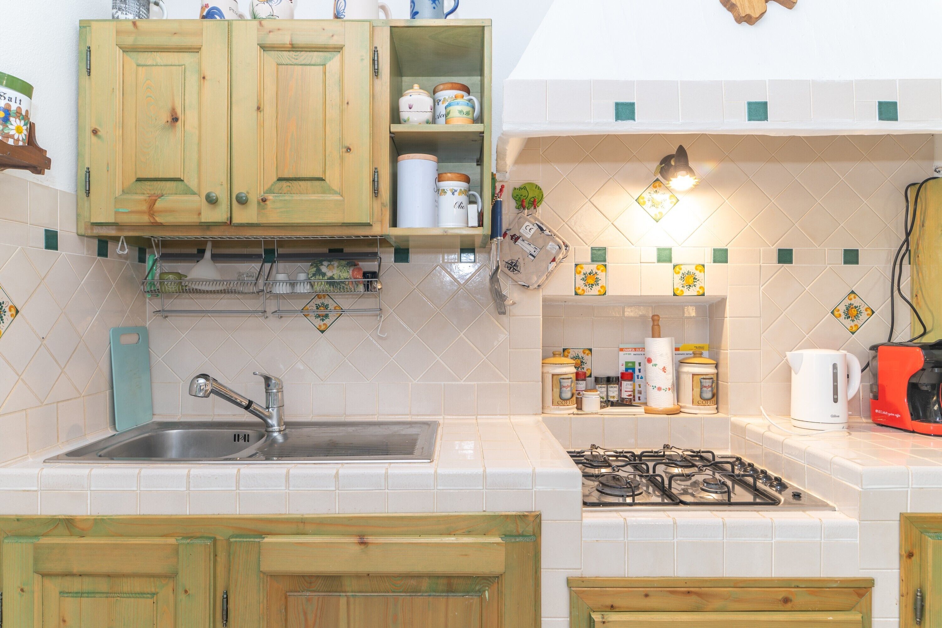 Una cucina con mobili in legno, un lavello in acciaio inossidabile, un fornello a gas e diversi utensili da cucina.